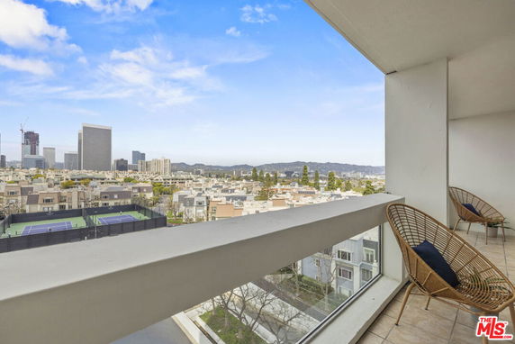 Balcony view overlooking cityscape with tennis courts and high-rise buildings.