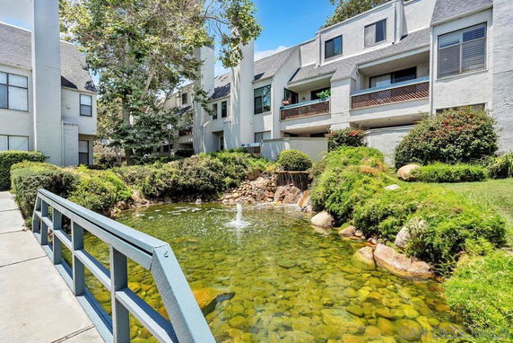 Front view of a multi-story residential complex with balconies and a pond in front.