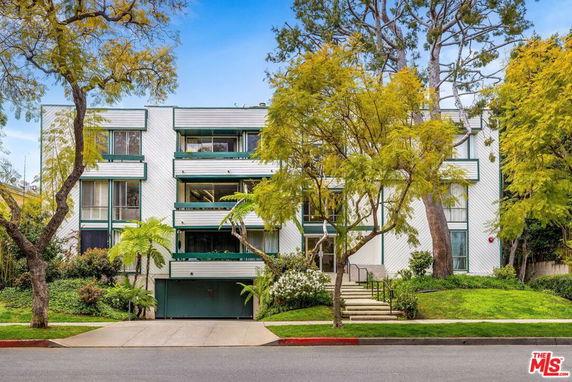 Front view of a multi-story apartment building with a tree-lined entrance.
