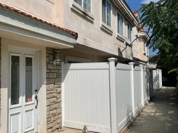 Front view of a multi-story building with a stone accent wall and a white entry door, alongside a privacy fence.