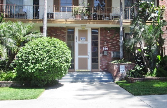 Front view of a brick building entrance with steps, potted plants, and a balcony.