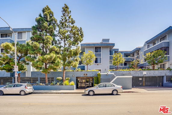 Front view of a multi-story residential building with trees in front and parked cars on the street.