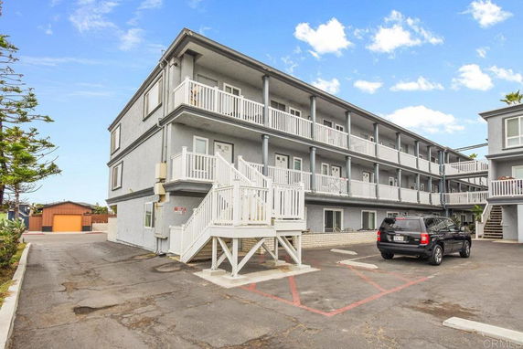 Front view of a three-story residential building with white railings and external staircases.