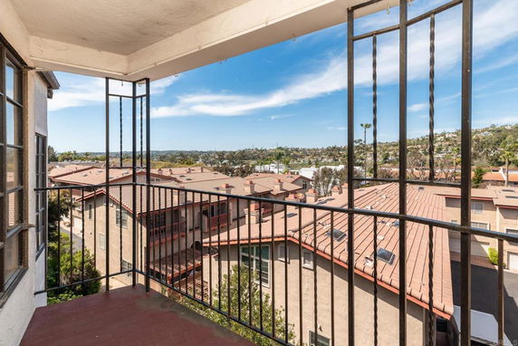 Panoramic view from a building balcony overlooking a residential area with multiple red-roofed houses.
