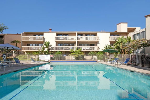 Swimming pool in front of a multi-story building with balconies and outdoor seating.