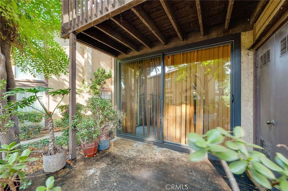 Outdoor view of a building's ground-level entrance with sliding glass doors and a shaded balcony above.