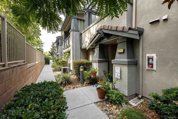 Front view of a multi-story residential building with a covered entrance and landscaped walkway.