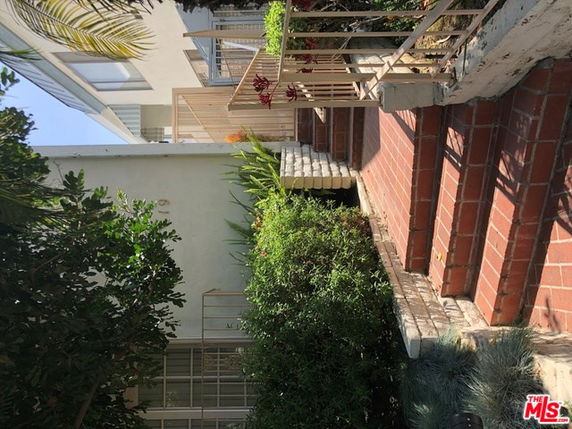 Front view of a house with brick steps and railing, surrounded by greenery.