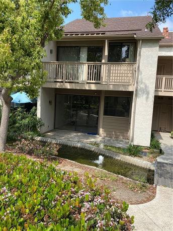 Front view of a two-story house with a balcony and a pond in front.