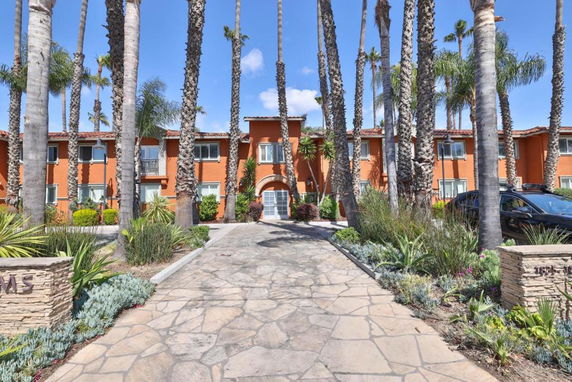 Front view of a two-story orange building surrounded by palm trees.