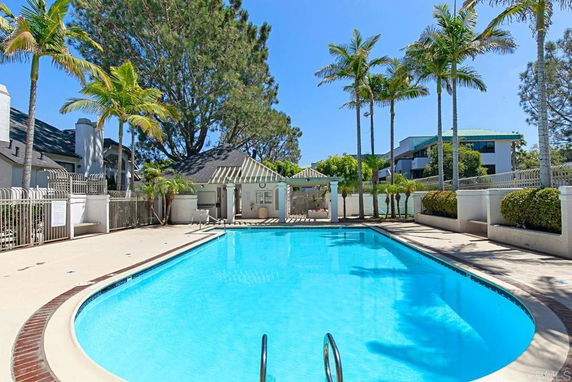 Outdoor swimming pool with surrounding palm trees and adjacent buildings.