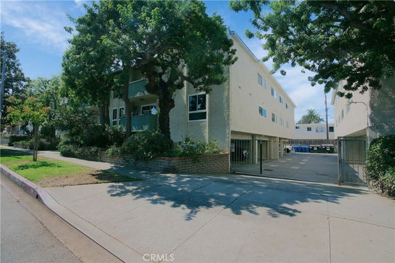 Front view of a multi-story apartment building with gated entrance and surrounding trees.