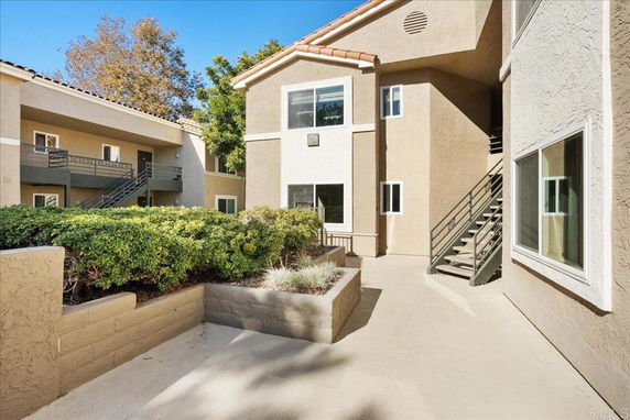 Front view of an apartment building with stairs and shrubbery.