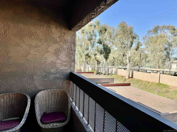 View from a building showing wicker chairs on a balcony and trees beyond a wall.