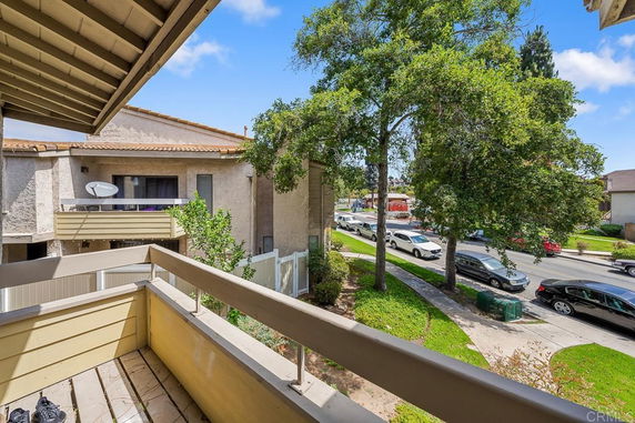 View from a balcony overlooking a residential street with parked cars and trees.