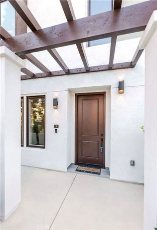Front view of a building entrance with a wooden door and pergola overhead.