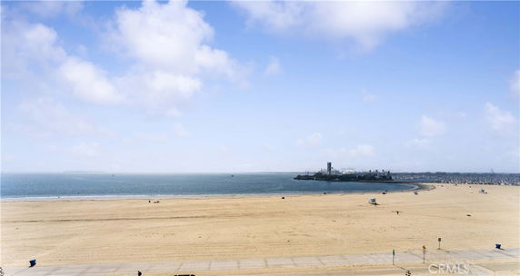 Panoramic view of a sandy beach and ocean with a distant cityscape in the background.