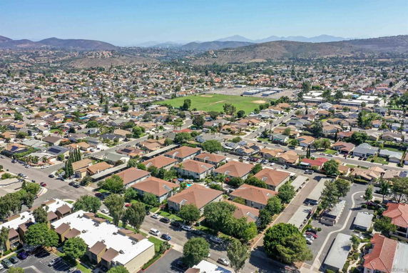 Aerial panoramic view of a residential neighborhood with rows of houses and green spaces in a hilly area.