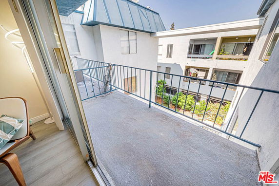 View from a balcony overlooking adjacent apartment buildings with visible balconies and greenery below.
