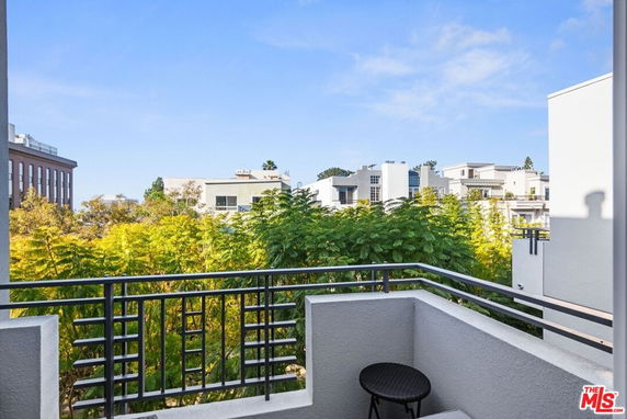 View of surrounding buildings from a balcony with greenery and a clear sky.