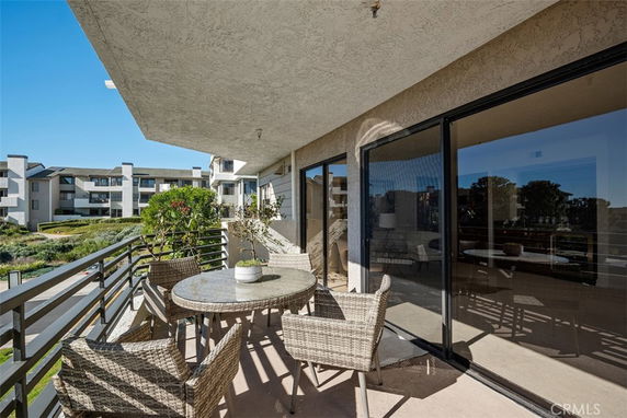Outdoor patio area with a table and chairs, overlooking adjacent buildings and greenery.
