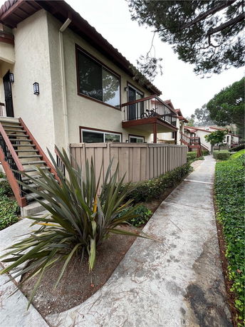 Side view of a multi-story residential building with balconies and a wooden fence.
