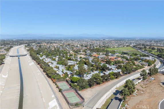 A panoramic view of a residential area with tennis courts, a canal, and distant mountains.