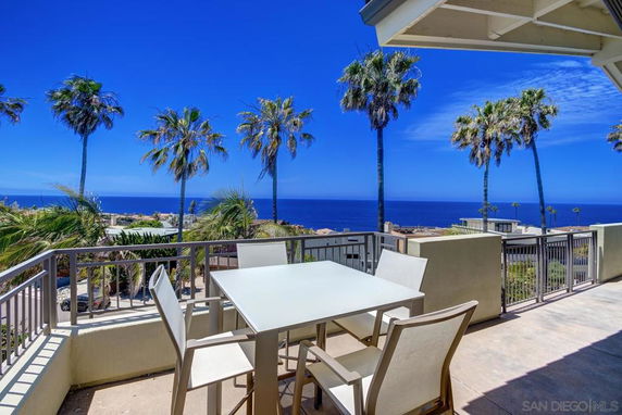 Outdoor patio with a table and chairs overlooking the ocean and palm trees.