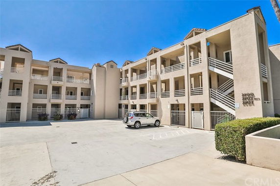Front view of a multi-story apartment building with open balconies and a parking area.