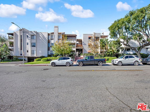 Front view of a multi-story apartment building with parked cars on the street.