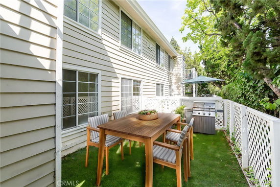 Side view of a house with outdoor seating and a grill on a grassed area.