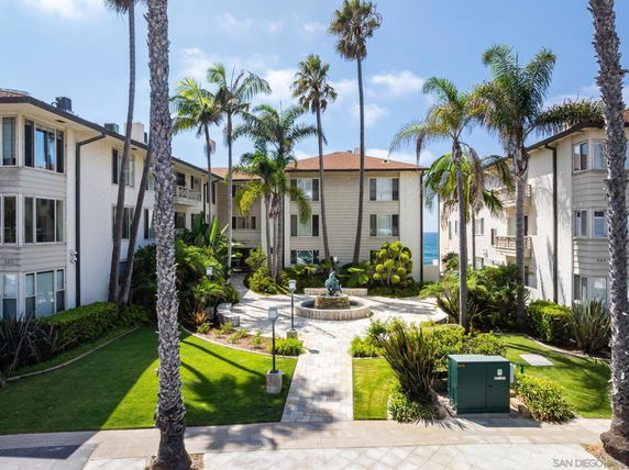 Complex of multi-story residential buildings with a central courtyard and palm trees.