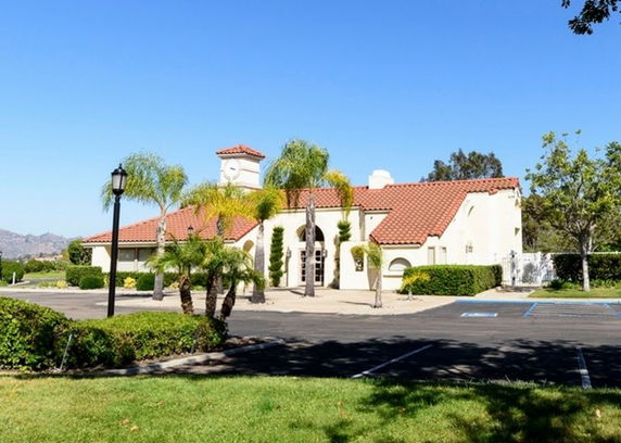 Front view of a building with red-tiled roof and palm trees in the foreground.