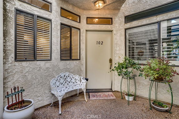Front view of a house entrance with a door labeled 102, surrounded by windows and decorative plants.