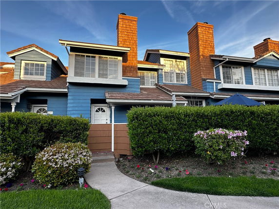 Front view of a two-story blue house with brown chimneys and white shutters.