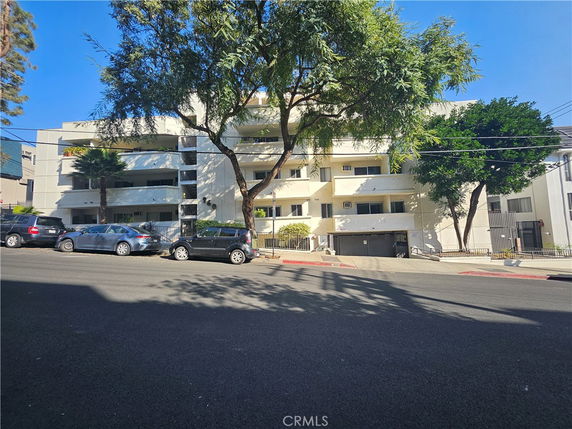 Front view of a multi-story residential building with balconies and street parking.