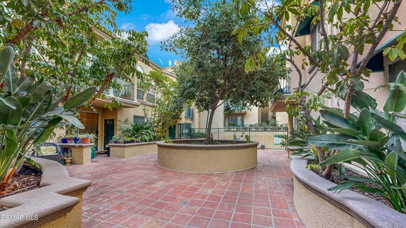 Outdoor courtyard area with plants and benches between residential buildings.