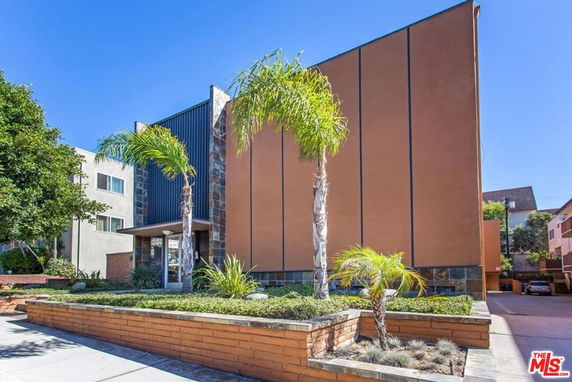 Front view of a modern multi-story building with a tall façade and surrounding palm trees.