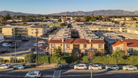 Aerial view of a neighborhood with multiple apartment buildings and a parking area, surrounded by mountains in the distance.