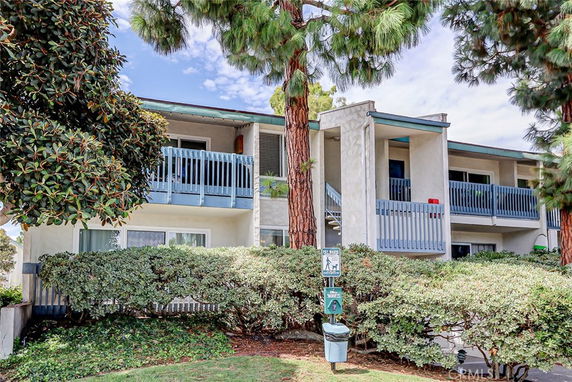 Front view of a two-story building with blue balconies and surrounded by trees.