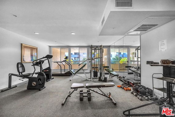 Room equipped with various gym equipment including exercise bikes, treadmills, and weights.