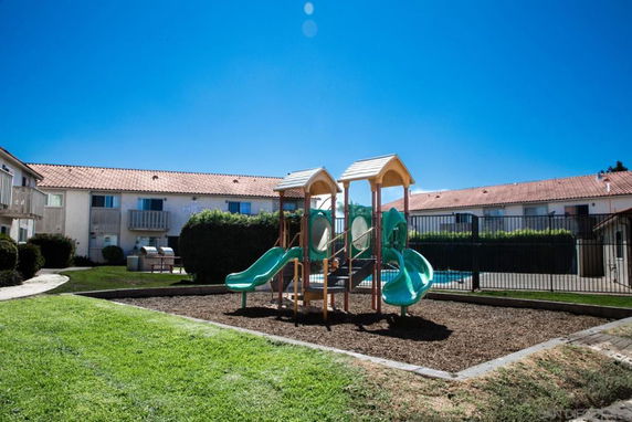 Playground with slides in an outdoor area surrounded by apartment buildings.