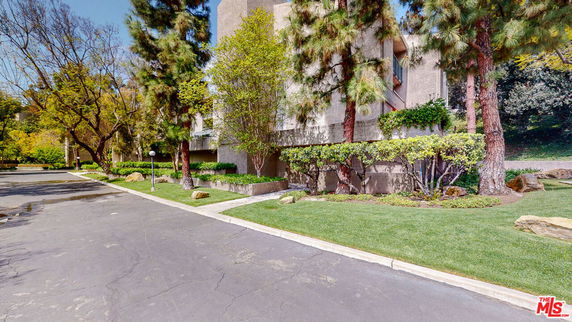 Front view of a multi-story building with trees and shrubs.