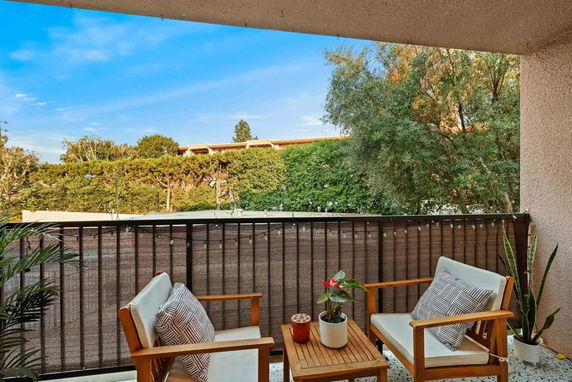 Balcony view with chairs and plants overlooking trees and a building in the distance.