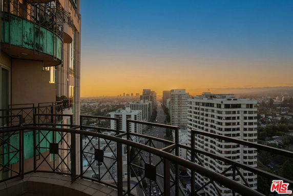 Panoramic view from a high-rise building balcony overlooking a city skyline at sunset.