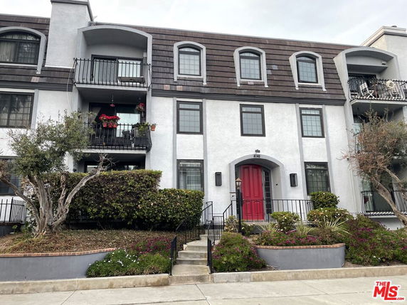 Front view of a multi-story building with balconies and a red entrance door.