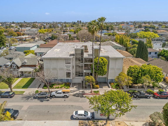 Aerial view of a multi-story building with a flat roof and large windows, surrounded by trees on a residential street.