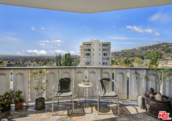 Panoramic view from a balcony showing a high-rise building and distant hills.