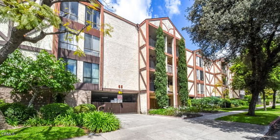 Front view of a multi-story building with a decorative facade and tall trees at the entrance.