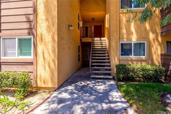Front view of an apartment building with staircase leading to upper level entrance.